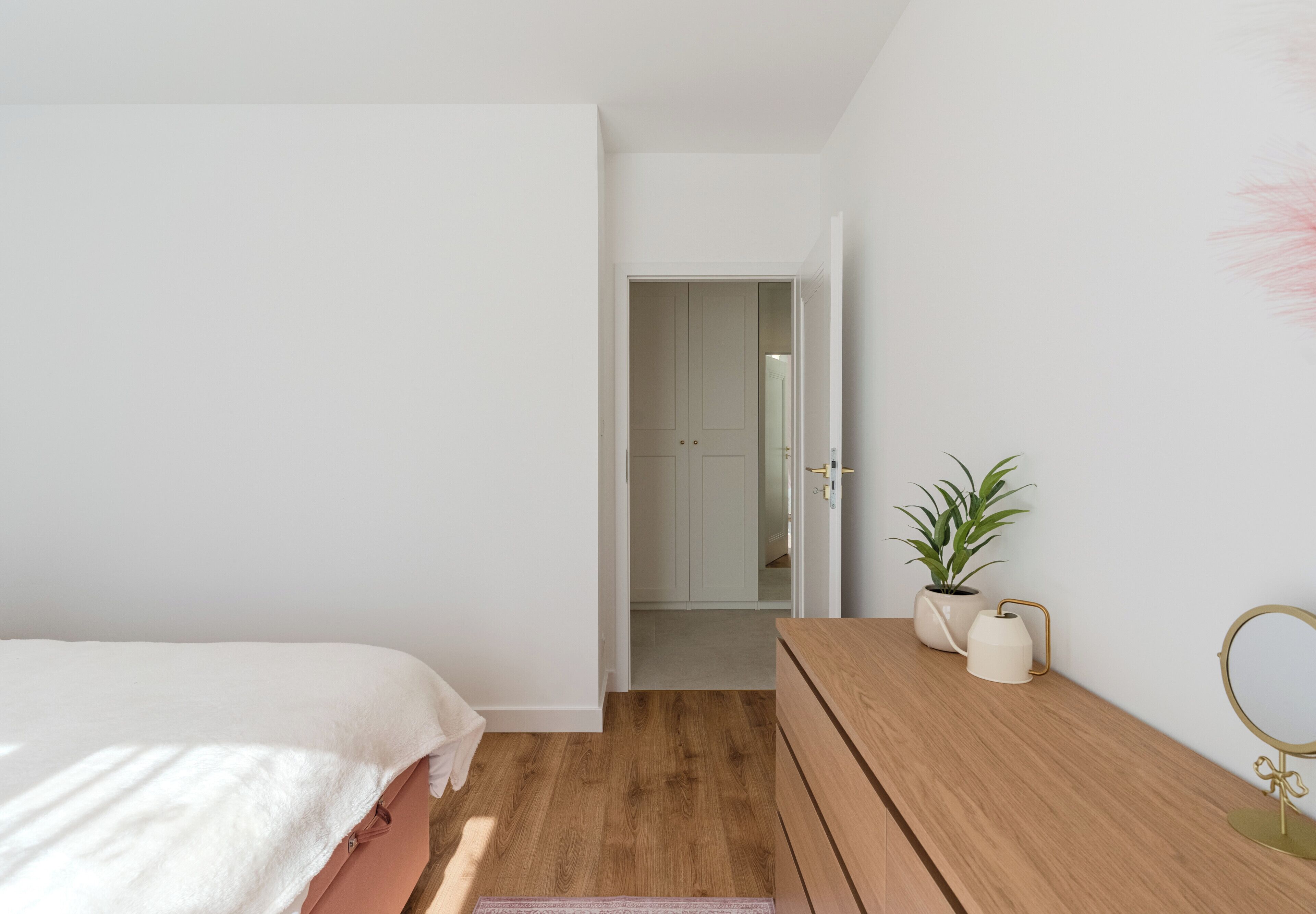 Un dormitorio con cama, cómoda de madera, planta en maceta y espejo.