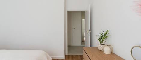 A bedroom with a bed, wooden dresser, potted plant, and a mirror.