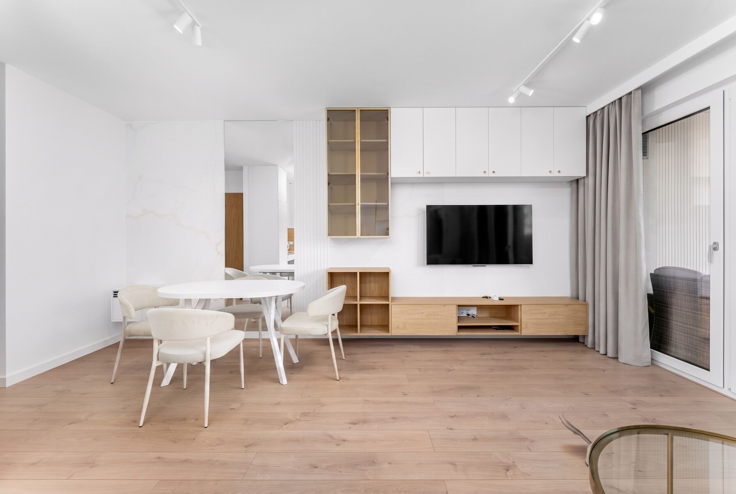 A modern living room with a flat-screen TV, white furniture, and a wooden floor.