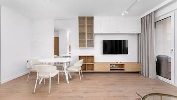 A modern living room with a flat-screen TV, white furniture, and a wooden floor.