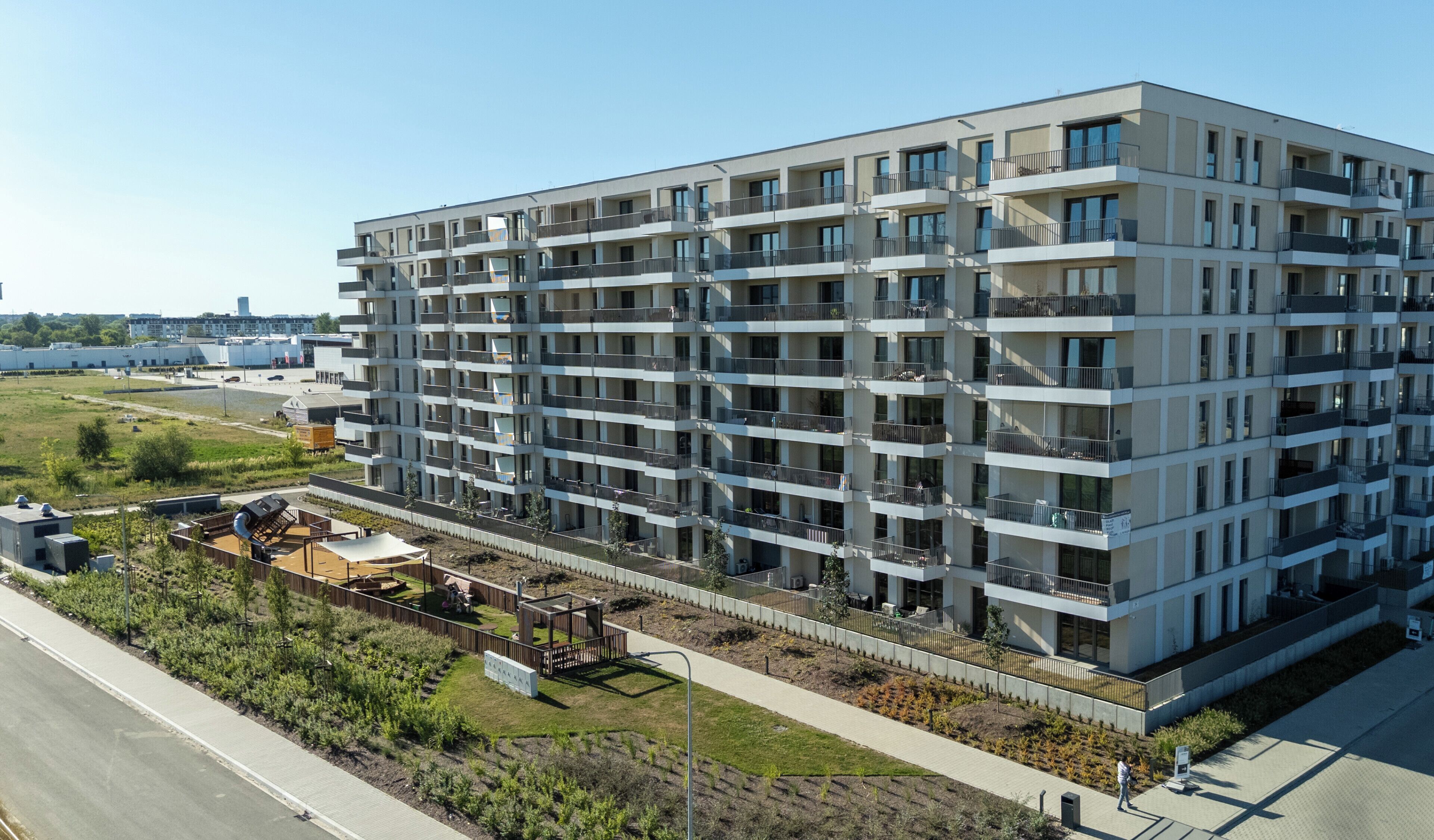 A multi-story residential building with balconies, a landscaped garden area, and a paved walkway.