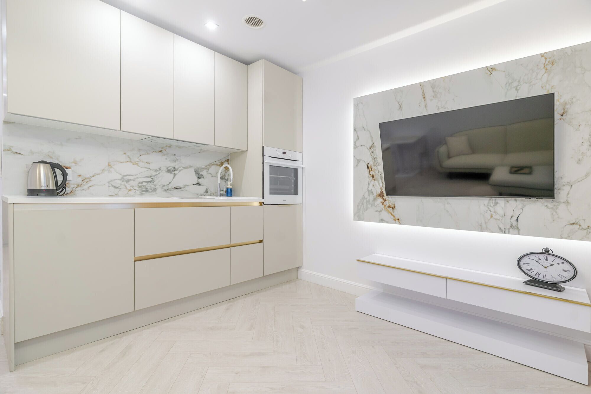 Una cocina moderna con armarios blancos, salpicadero de mármol y horno empotrado.