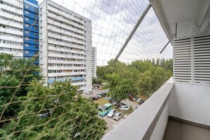 A high-rise building with multiple floors, a parking area with cars, and a dense tree line in the foreground. - Piastów Homely Apartment (Katowice)