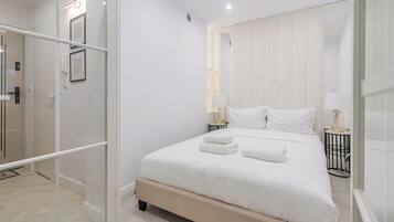 Un dormitorio moderno con una cama grande, lámparas de noche y una cabina de ducha de vidrio.
