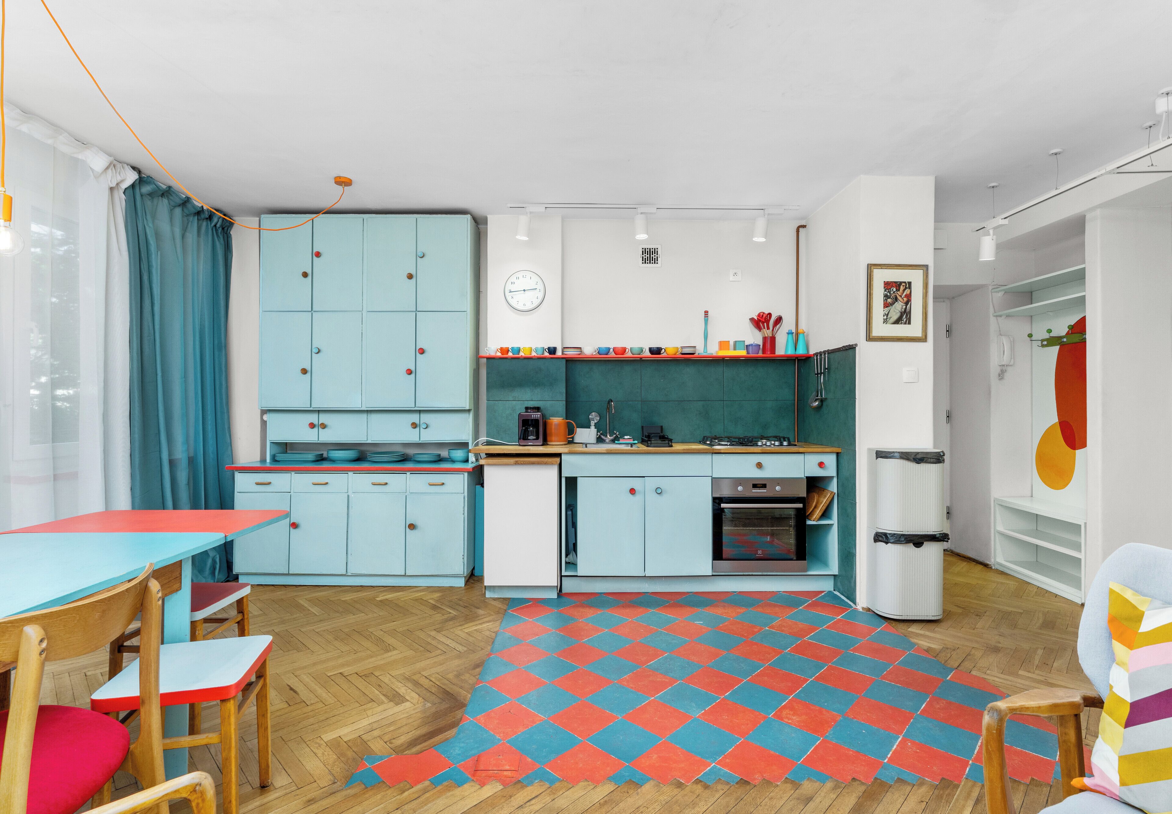 Une cuisine compacte avec un sol à motifs en chevrons, une table à manger avec des chaises et une horloge au mur.