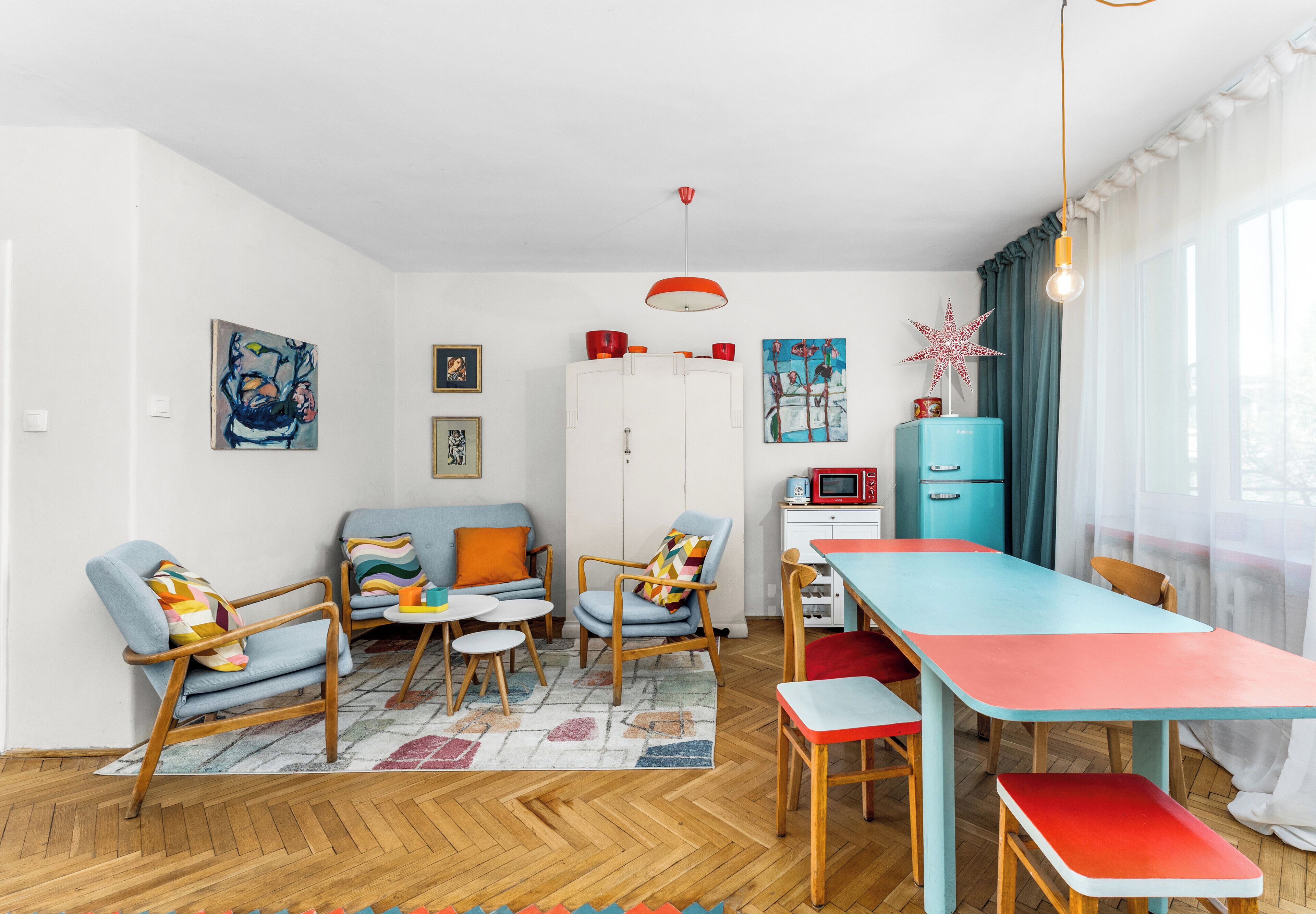 A modern living room with a sofa, chairs, a dining table, and a kitchen area with a fridge and microwave.