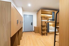 A compact hotel room with a bunk bed, wooden wardrobe, and a door.