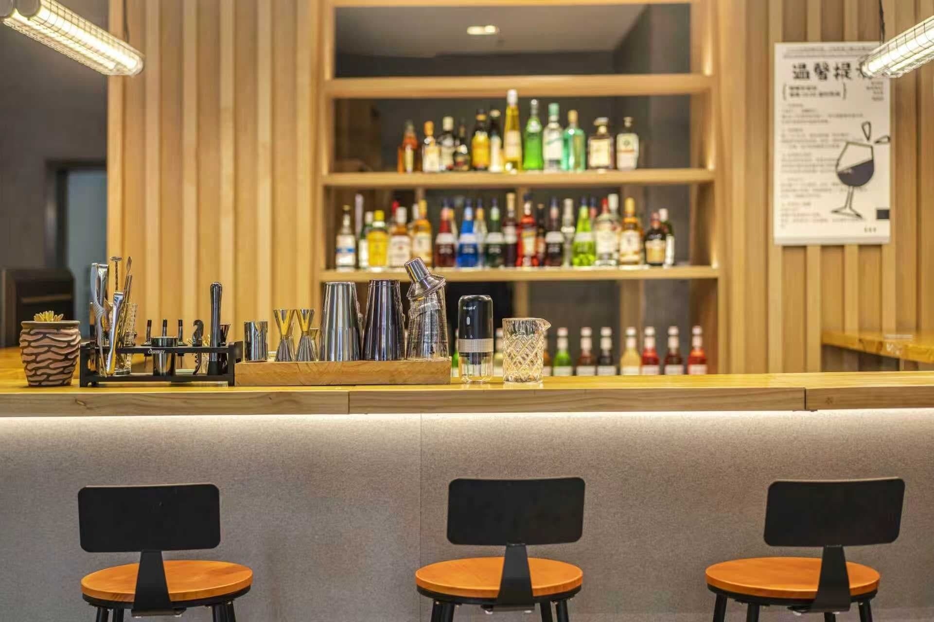 A bar area with a counter, various bottles, and barware. There are three chairs in front of the bar.