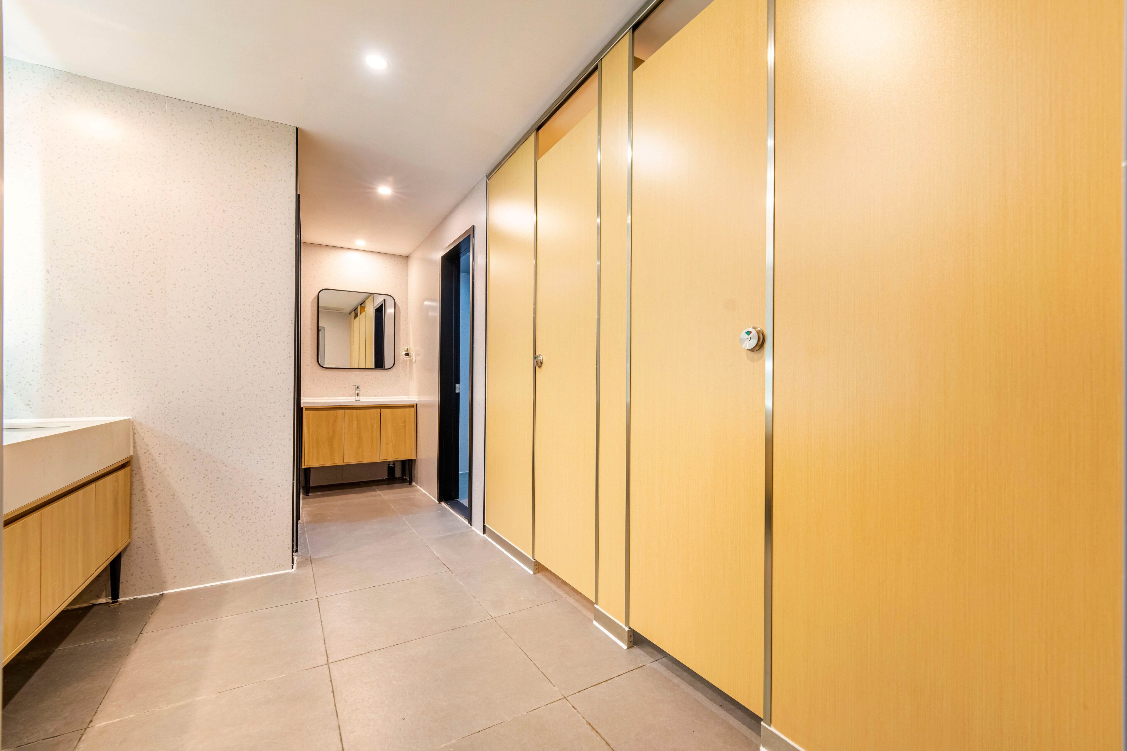 A hallway with a mirror, a sink, and wooden cabinets.
