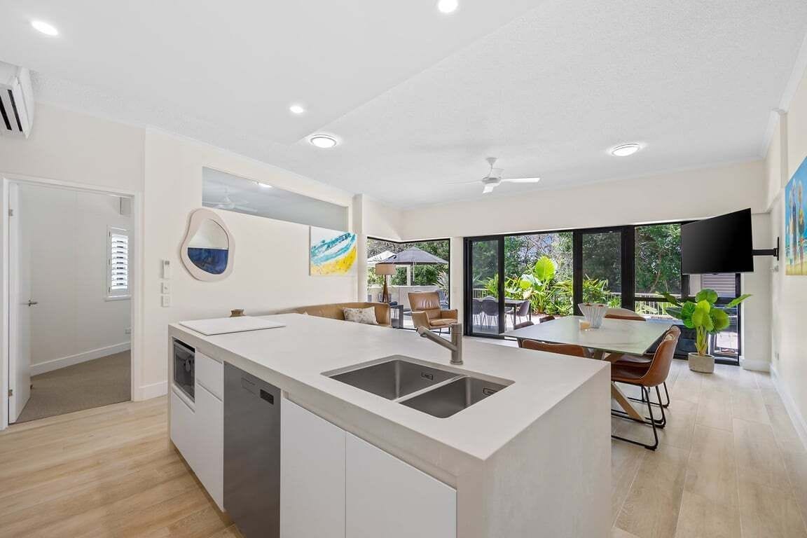 A modern kitchen with a central island, a dining area with a table and chairs, and a large window providing a view of the outdoors.
