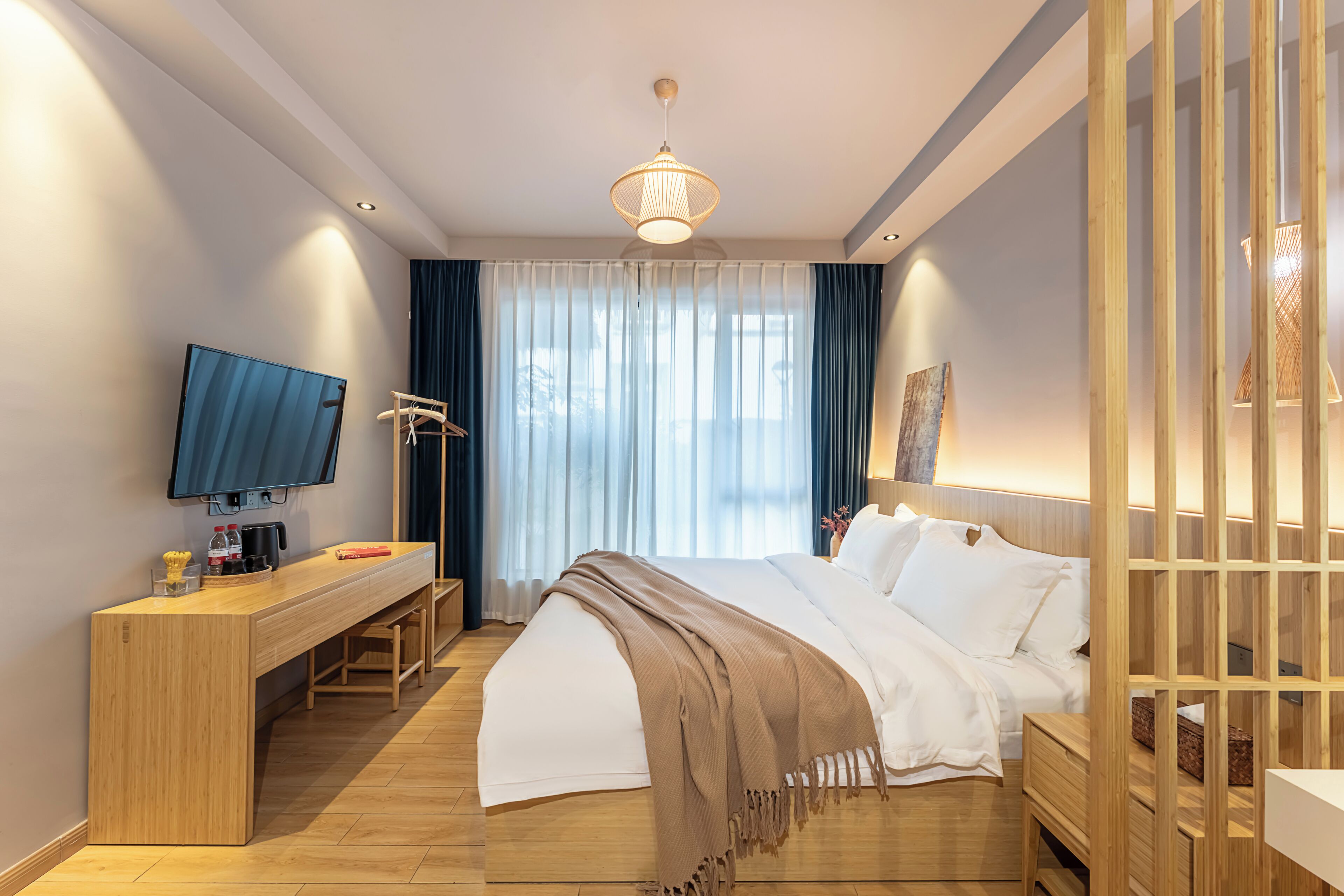 A hotel room with a bed, a desk with a television, a chair, and a large window with curtains.