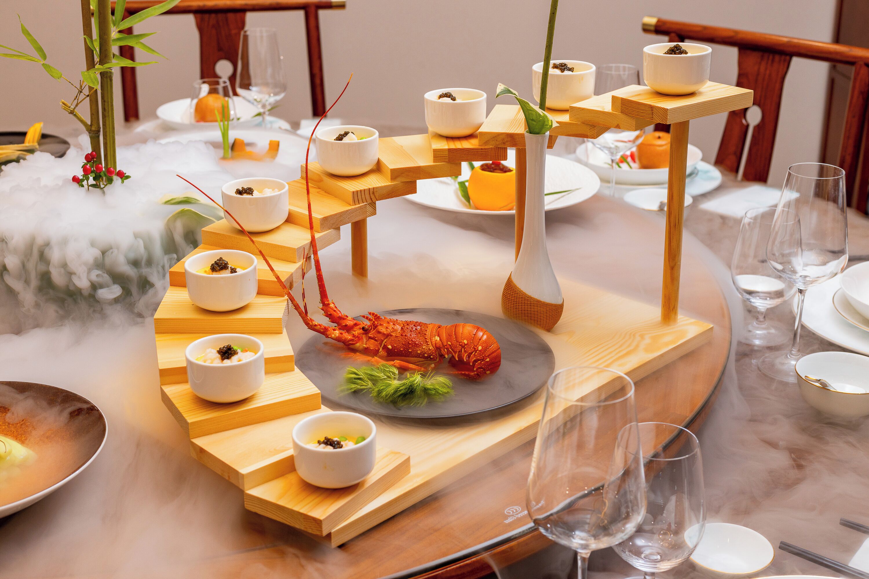 A round dining table with a lobster centerpiece, multiple small bowls, and a bamboo plant.