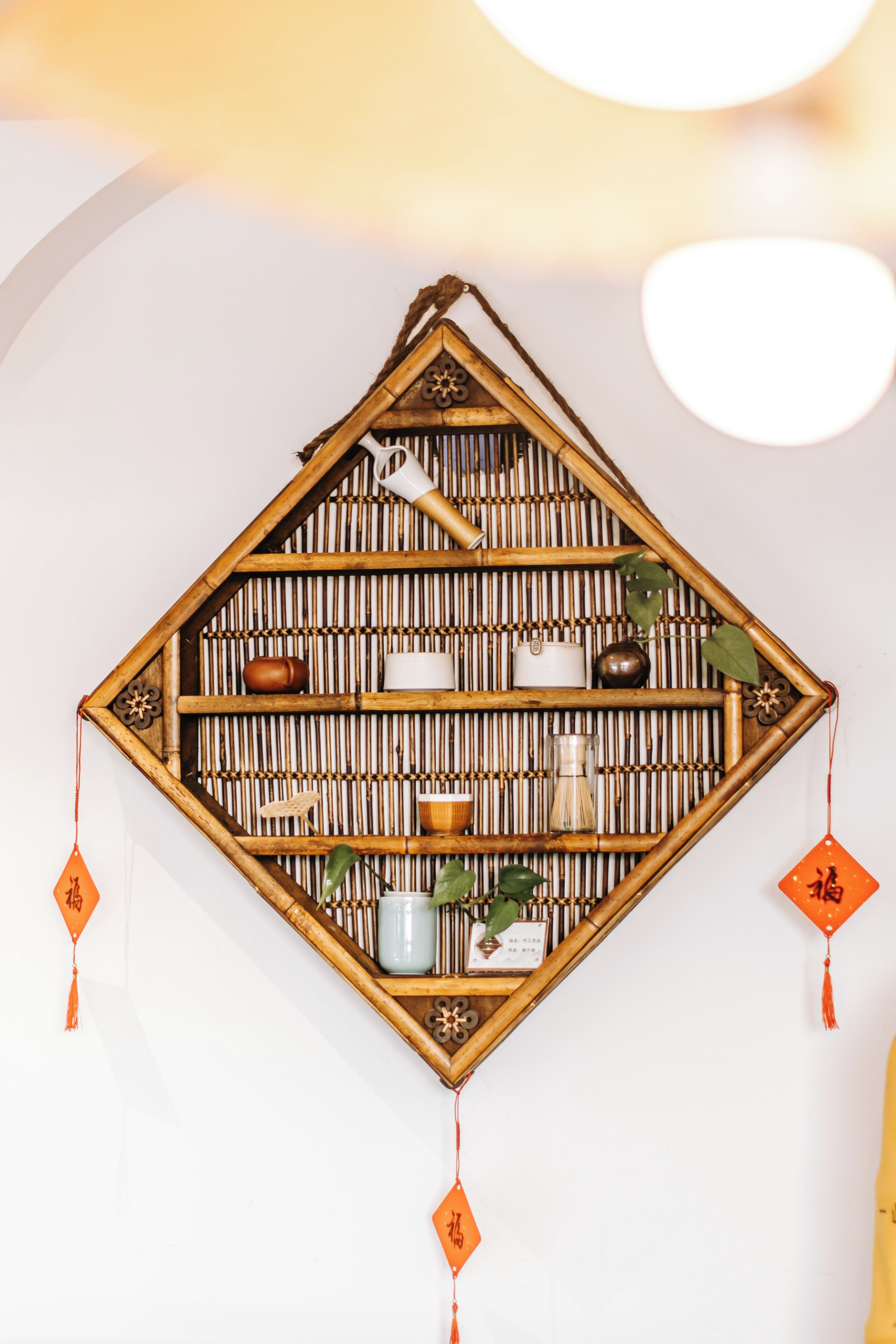 Estante decorativo montado en la pared con estructura de bambú, que contiene varios objetos como una tetera, tazas y una planta pequeña.