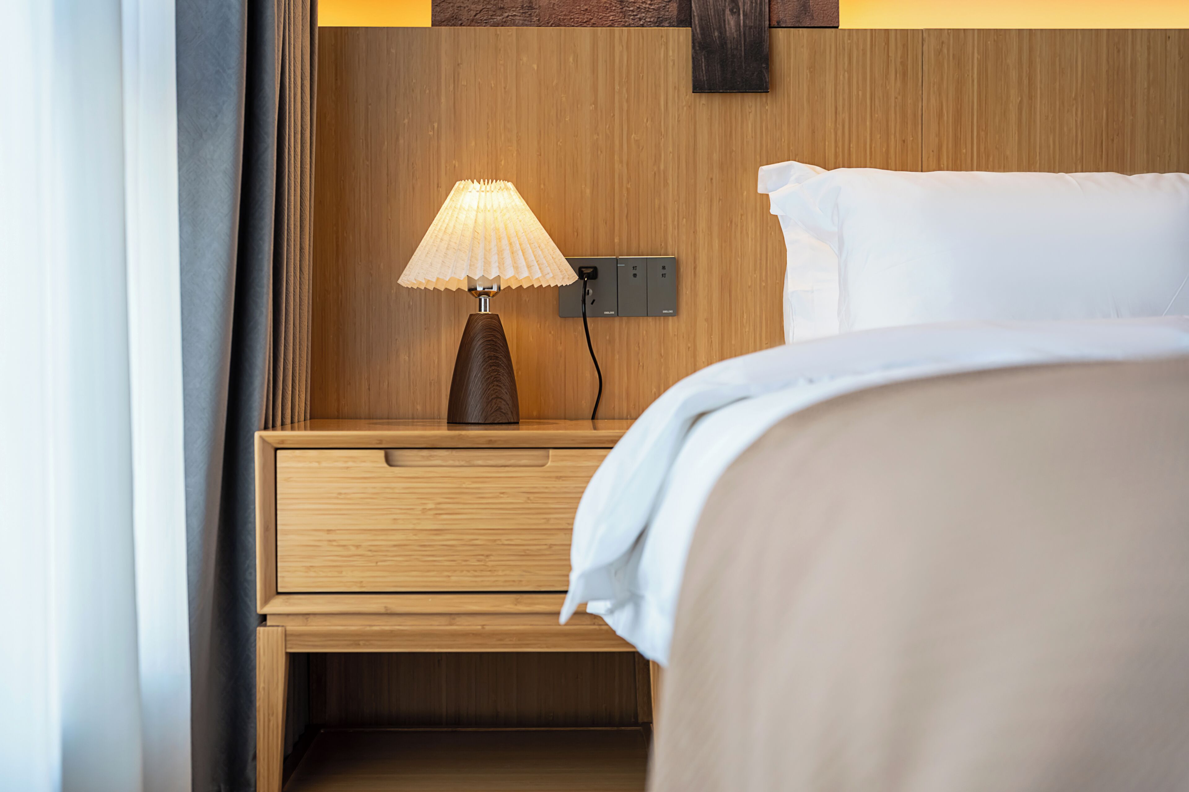 Cama bem arrumada com travesseiro branco e mesa de cabeceira de madeira com abajur.