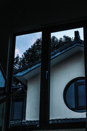 A window with a view of a building's exterior, including a roof and trees.