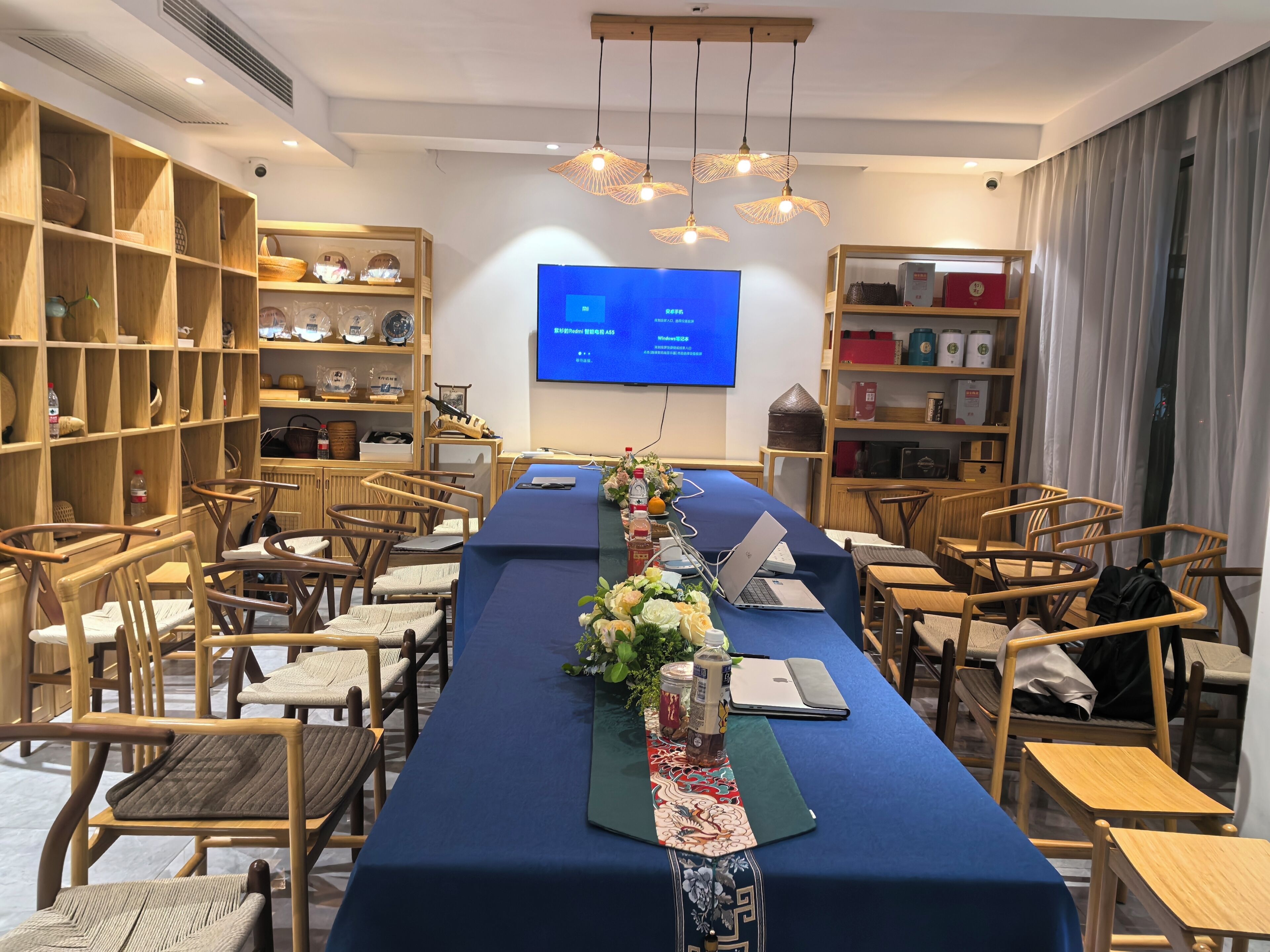 A conference room with a long table, chairs, a screen, and shelves with various items.