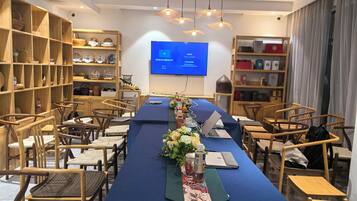 A conference room with a long table, chairs, a screen, and shelves with various items.