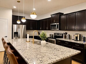 Une cuisine moderne avec des meubles de couleur sombre, des appareils en acier inoxydable, un plan de travail en granit et des luminaires suspendus.