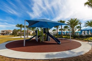 A playground with a slide and climbing structures, surrounded by a red play area and a blue canopy. - Luxury 8BR 6BA Villa with Heated Pool, Spa, Themed Rooms, and EV Charger (Kissimmee)