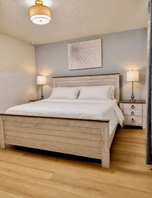 Une chambre à coucher avec un lit en bois, deux tables de chevet avec des lampes, un luminaire fixé au mur et un ventilateur de plafond.
