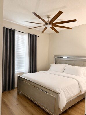 Una camera da letto con un letto, tende, un ventilatore a soffitto e una finestra con persiane.