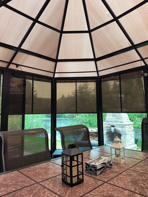 A covered patio area with a stone fireplace, seating, and a view of the outdoors. - Waterfront Cabin | Spa | Fireplaces | Gazebo (Bowman)
