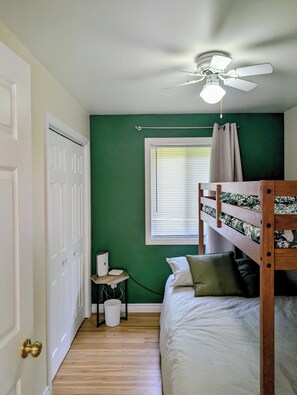 A room with a bunk bed, a ceiling fan, a window with blinds, a white door, and a small table with a lamp. - Waterfront Cabin | Spa | Fireplaces | Gazebo (Bowman)