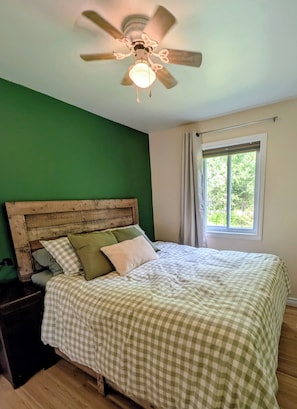 A bedroom with a wooden headboard, a checkered bedspread, a ceiling fan, and a window with curtains. - Waterfront Cabin | Spa | Fireplaces | Gazebo (Bowman)