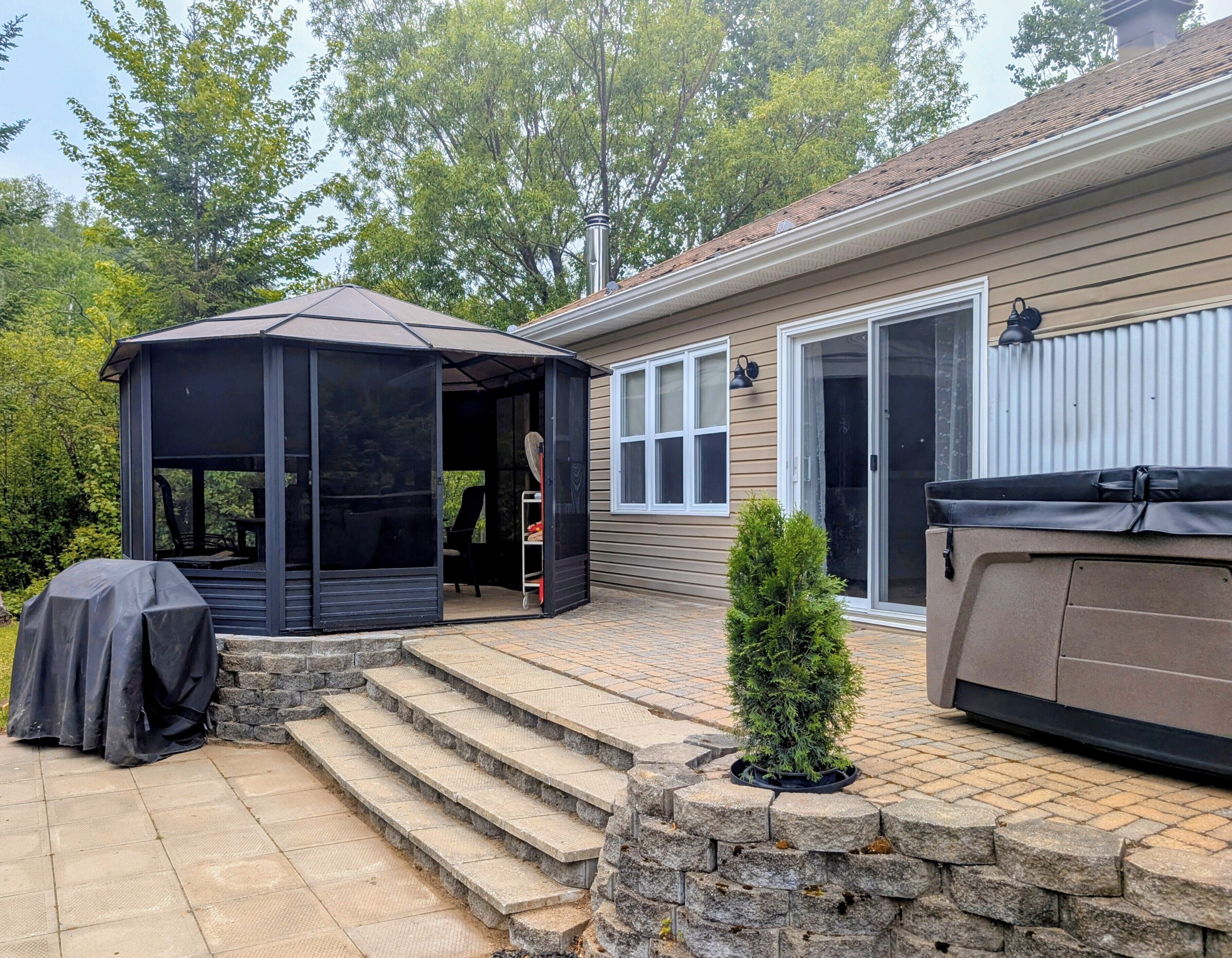 A covered patio area with a hot tub, a small gazebo, and a stone wall.