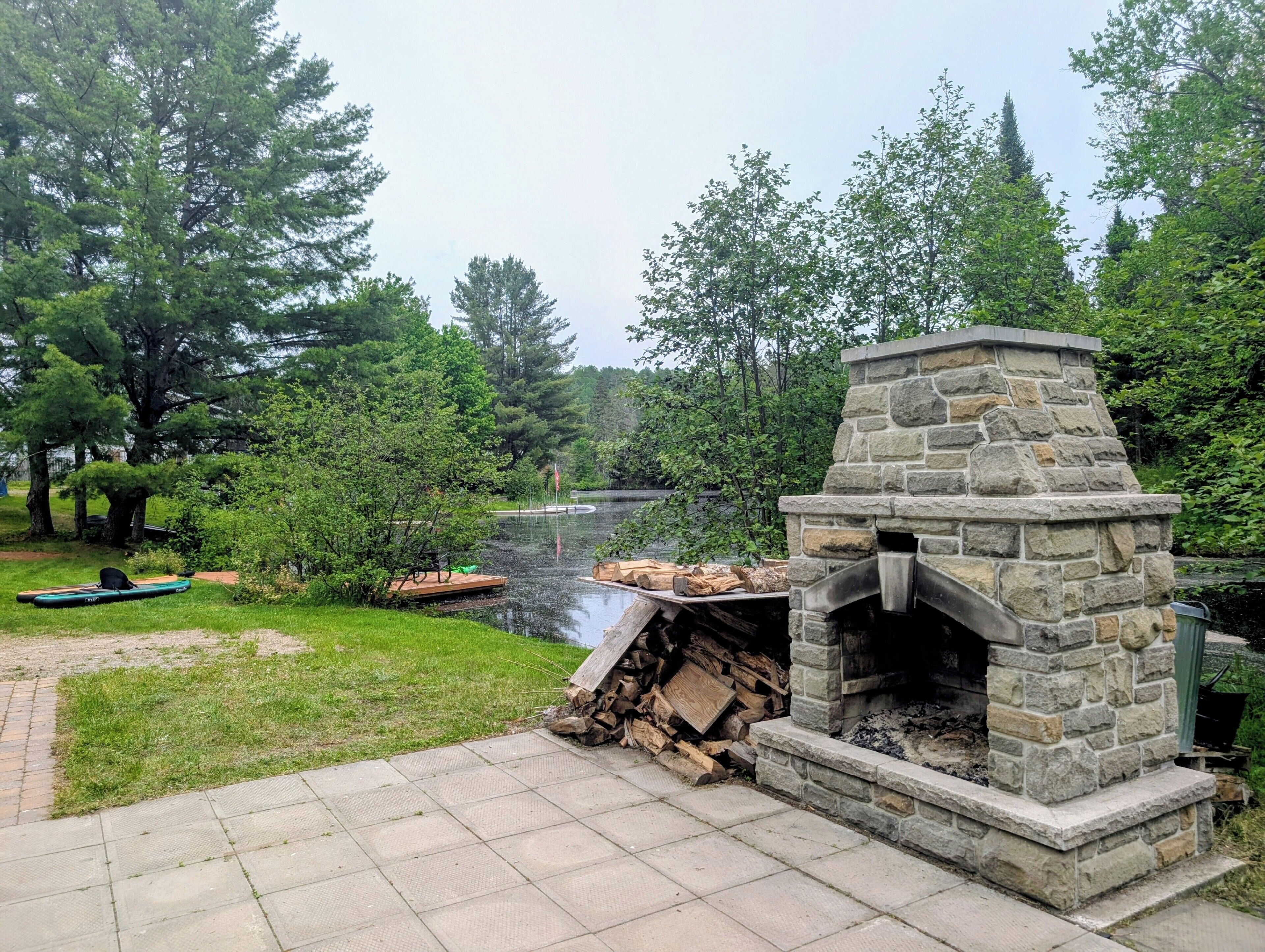 A stone-built outdoor fireplace with a fire pit, surrounded by a grassy area and a body of water.