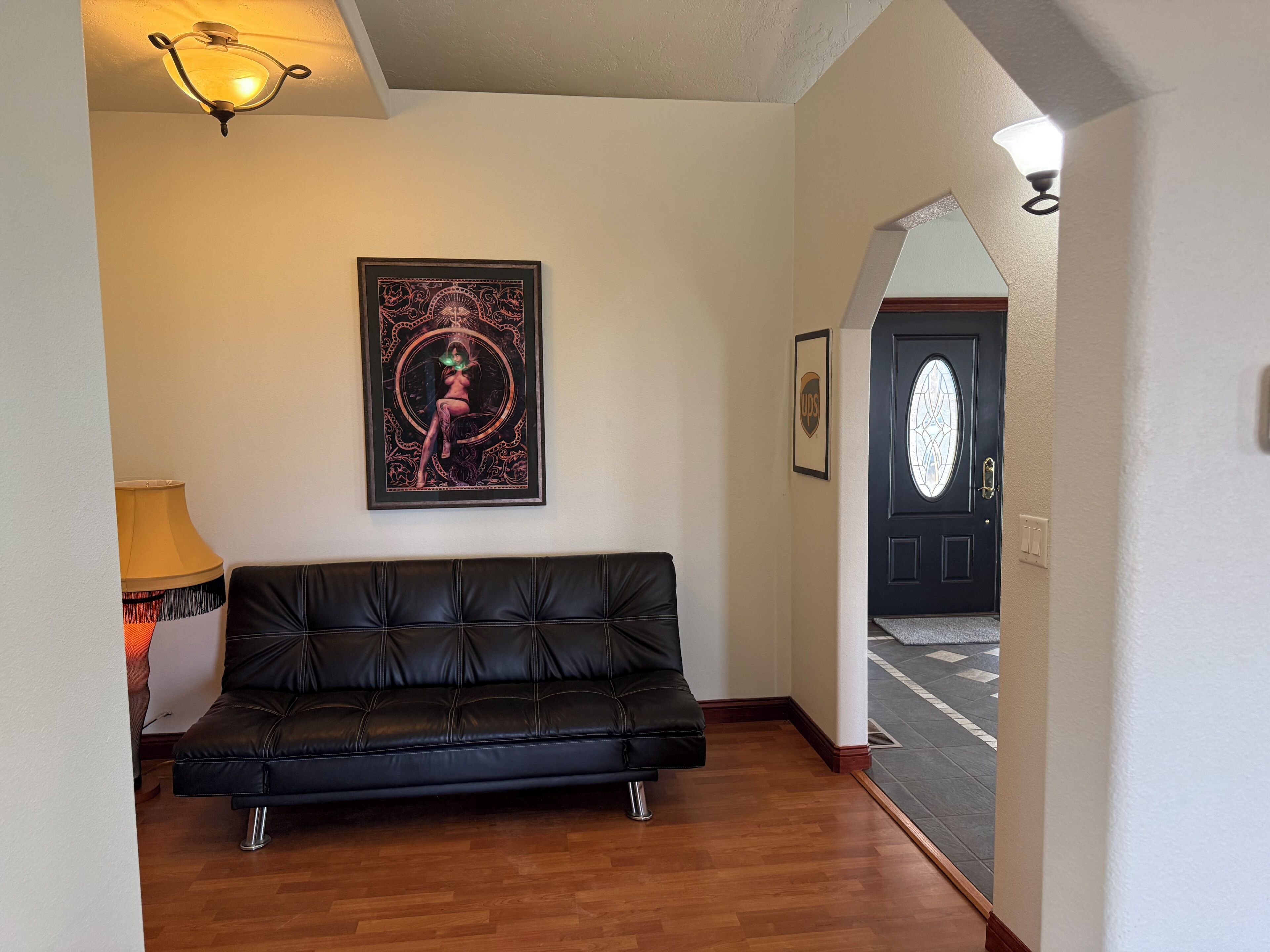 A black leather sofa in a hallway with a framed artwork on the wall, a lamp, and a UPS logo on the door.