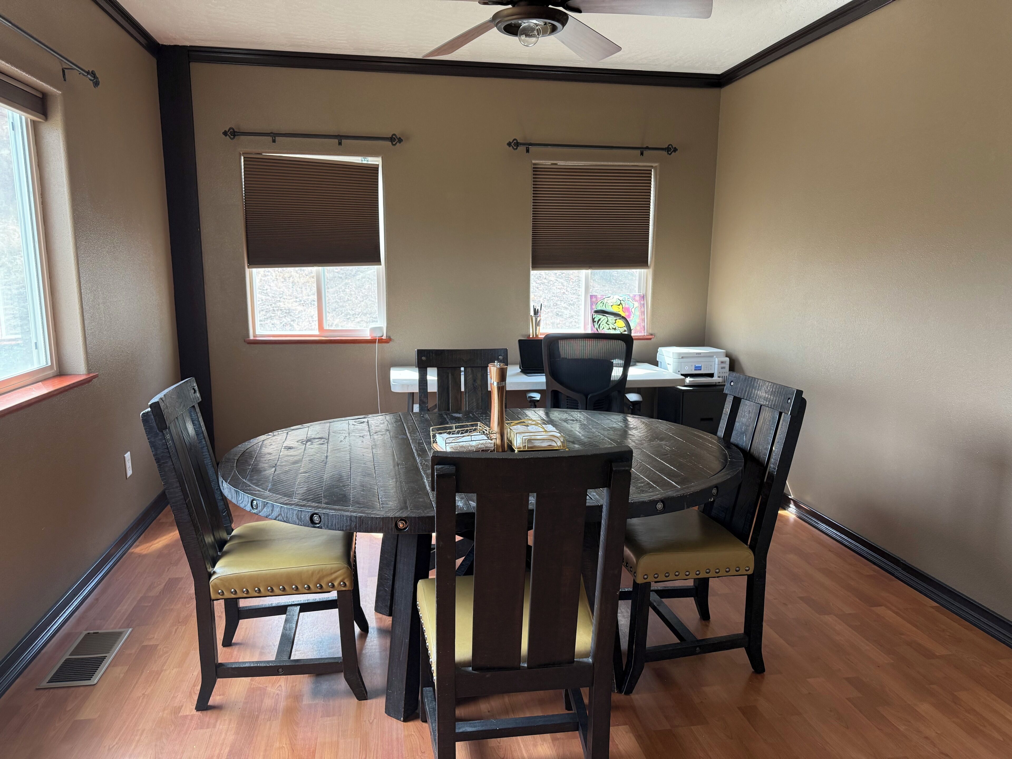 A dining area with a round table, six chairs, and a ceiling fan.