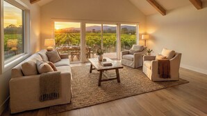 Amplio salón con techo alto, ventanas grandes y vistas a un viñedo.