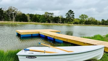 Een kleine witte boot met een blauwe vlag, afgemeerd aan een houten steiger die het water in reikt, omgeven door groen.