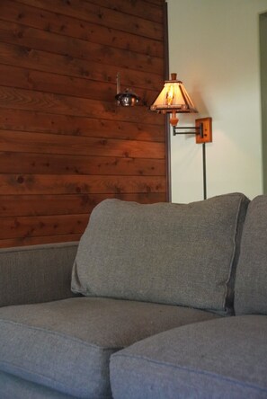 Un canapé gris adossé à un mur en bois, avec un lampadaire à proximité.