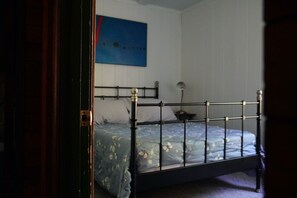 Une chambre avec un lit en métal, une couvre-lit à motifs floraux bleus, une lampe fixée au mur et un tableau abstrait bleu.