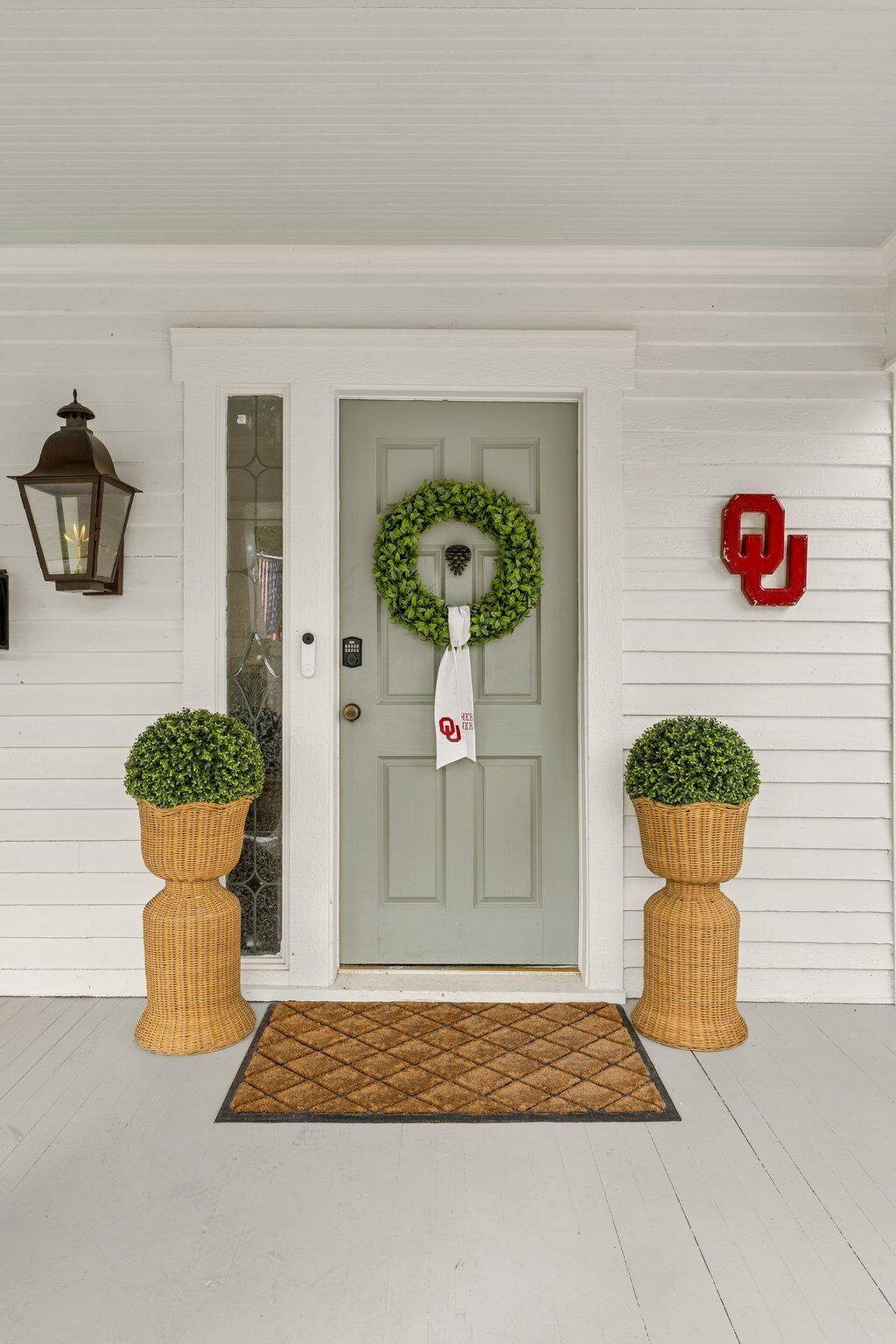 A front door with a wreath, a doormat, a lantern, and two potted plants.