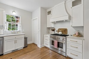 Una cocina con armarios blancos, estufa de acero inoxidable y tabla de cortar de madera.