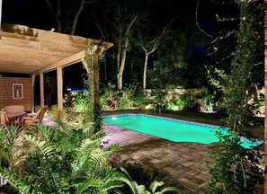 Ein Poolbereich im Freien bei Nacht mit einer Holzterrasse und Liegestühlen.