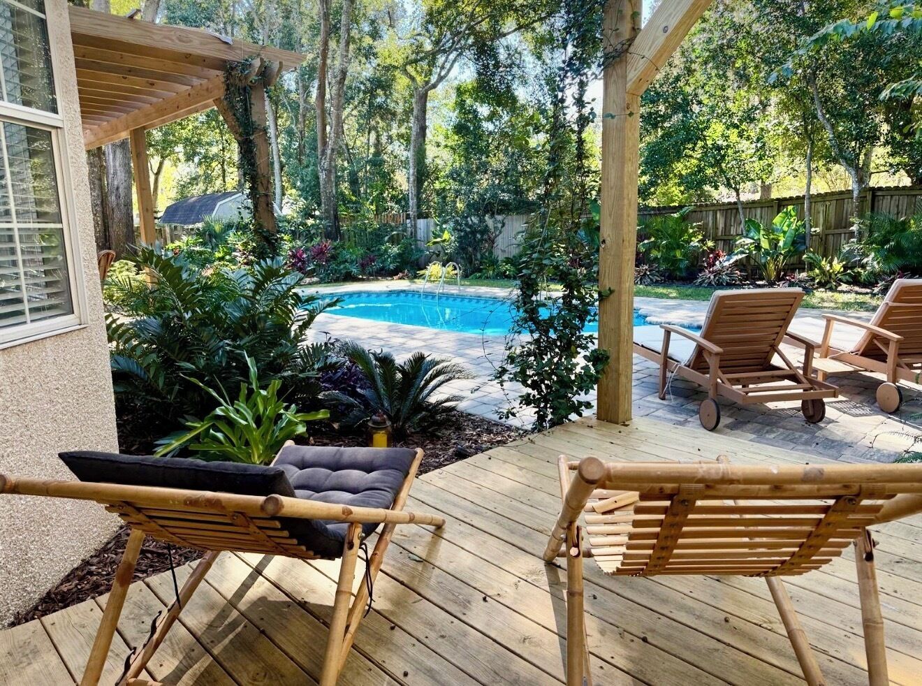 Une terrasse en bois avec deux chaises longues, une piscine et une végétation luxuriante.