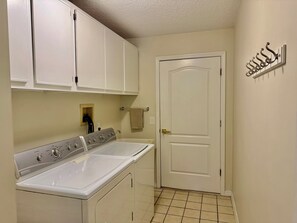 A laundry room with a front-loading washer and dryer, white cabinets, a door, and a towel rack. - Beautiful Pool Home near Beaches and Downtown (St. Augustine)