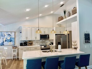 A modern kitchen with white cabinets, a marble countertop, and a central island with bar seating. - Beautiful Pool Home near Beaches and Downtown (St. Augustine)