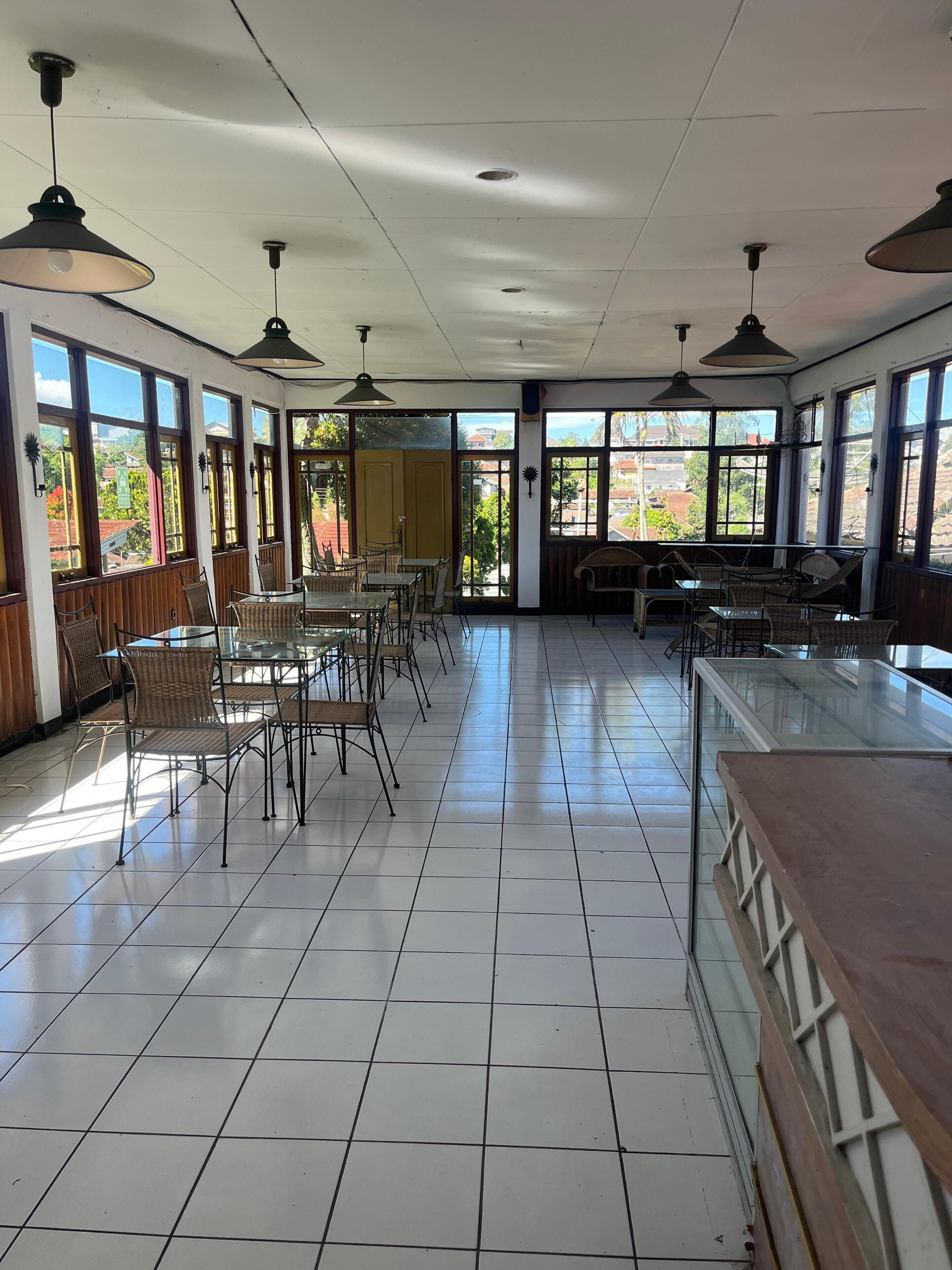 Un amplio espacio interior con suelo de baldosas, varias mesas y sillas, y ventanas grandes que ofrecen vistas al exterior.