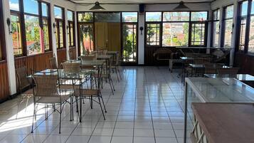 Un amplio espacio interior con suelo de baldosas, varias mesas y sillas, y ventanas grandes que ofrecen vistas al exterior.