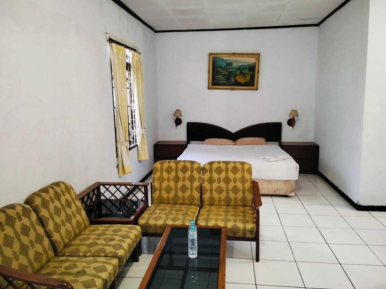 Ein Hotelzimmer mit einem Bett, zwei Sesseln, einem Sofa, einem kleinen Tisch, einem Bild an der Wand und einem Fenster mit Vorhängen.