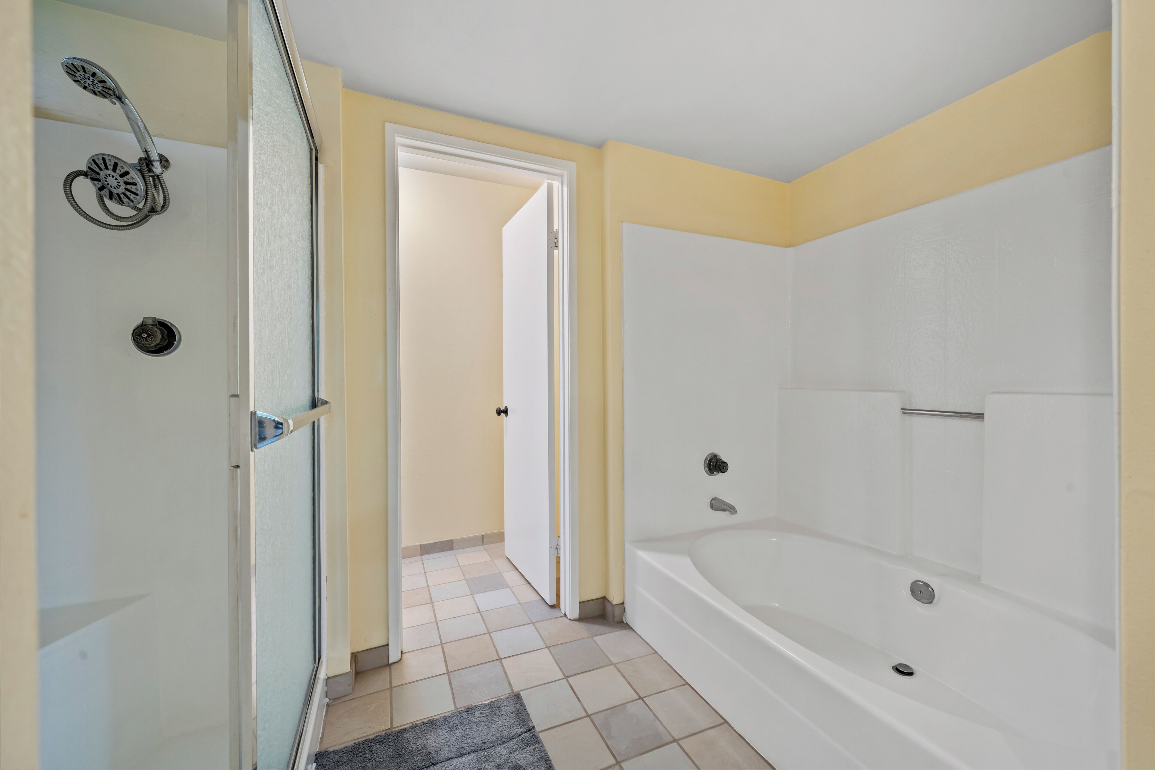 A bathroom with a shower, a bathtub, and a door leading to another room.