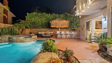 A pool area with a hot tub, outdoor seating, and a covered umbrella.