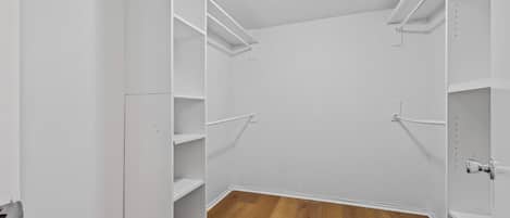 A walk-in closet with white shelving units and a wooden floor.