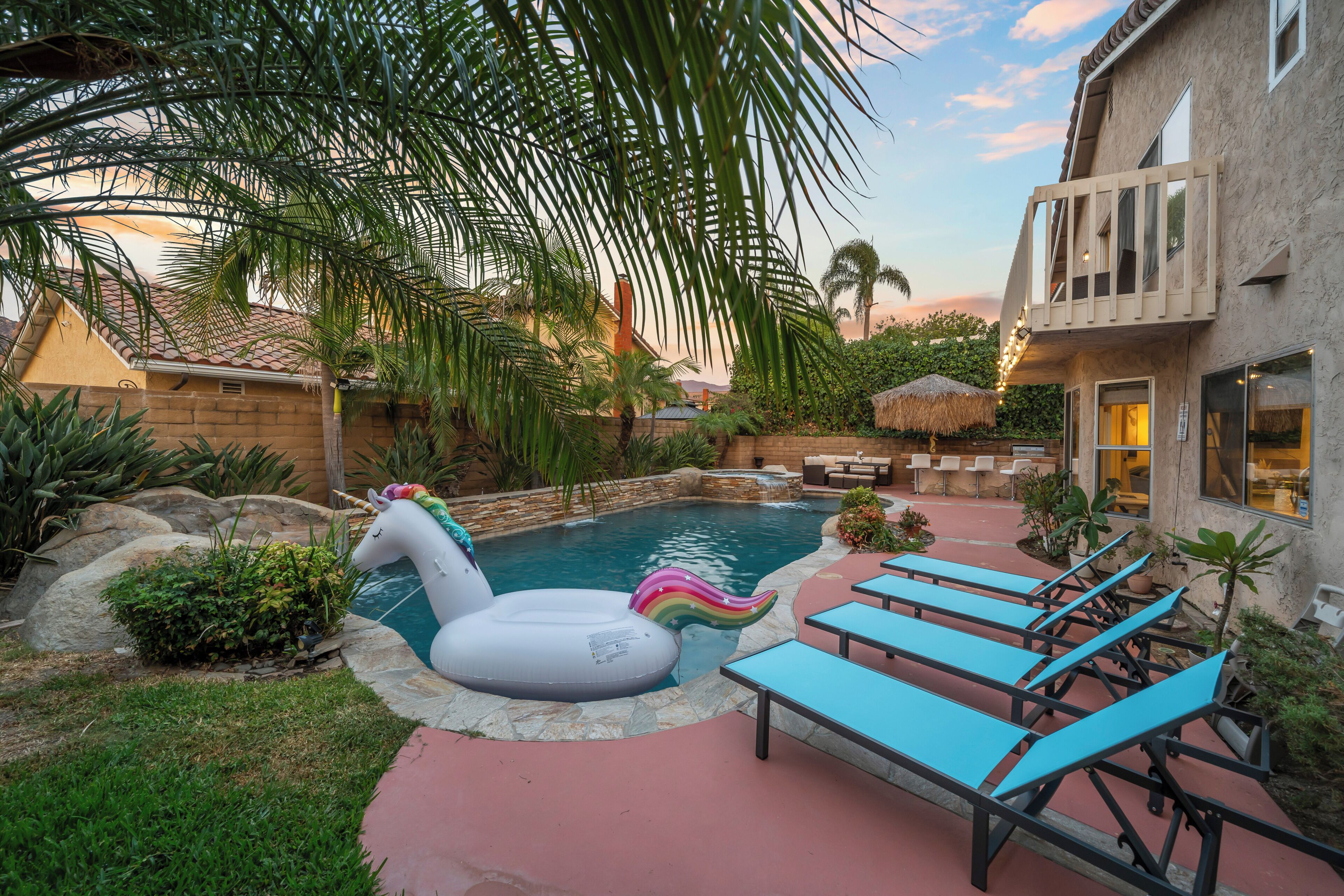 Ein Swimmingpool mit einem Einhorn-Schwimmtier, Liegestühlen und einem Reetdach-Sonnenschirm.