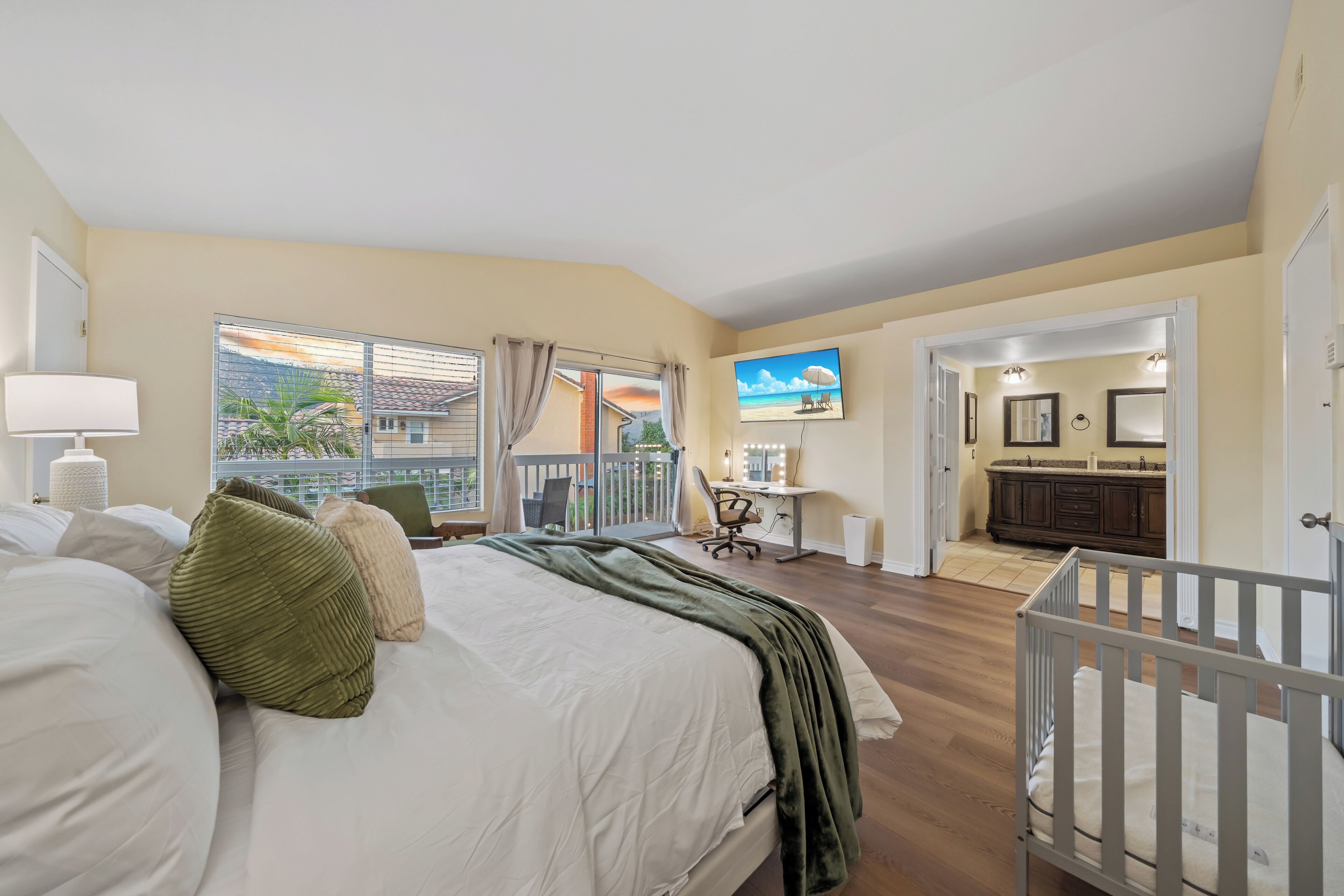 Ein Schlafzimmer mit einem großen Bett, einem Schreibtisch, einem Babybett und einem Balkon mit Blick auf den Strand.